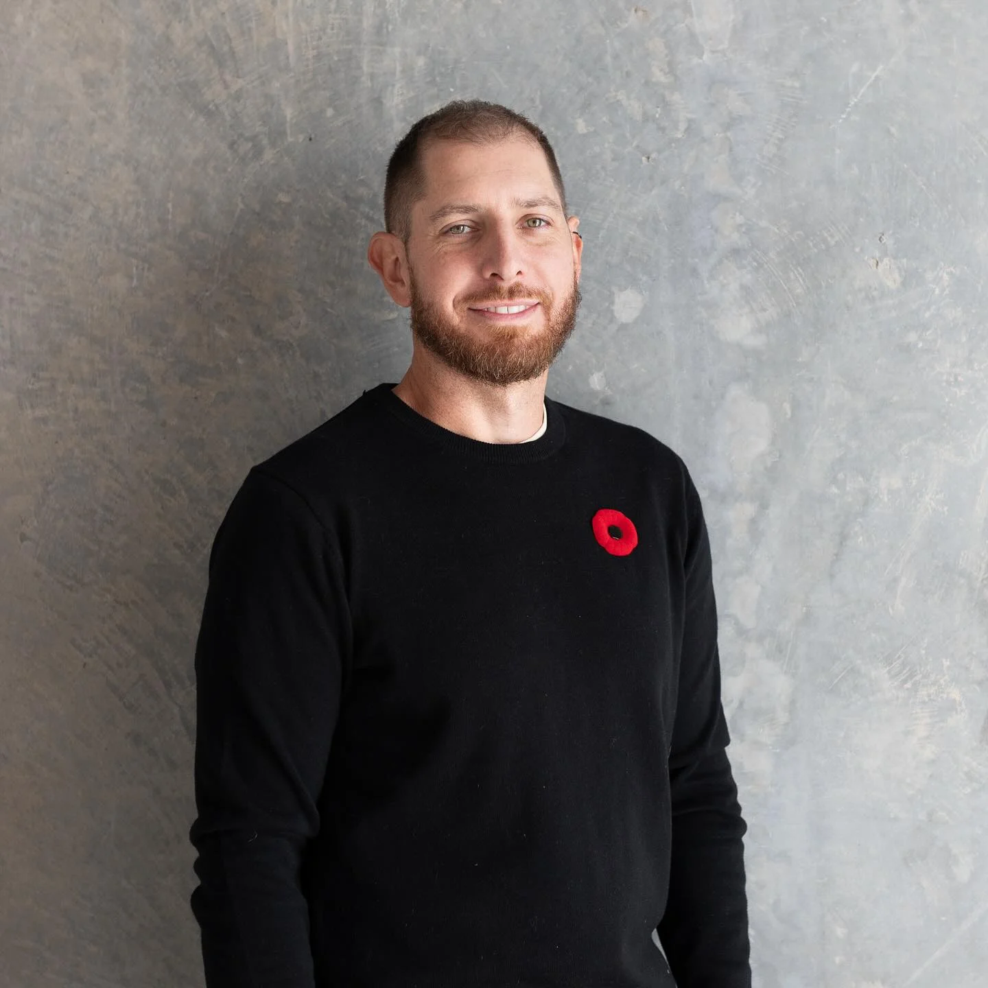 Smiling man with beard wearing black sweater standing in front of textured concrete wall background